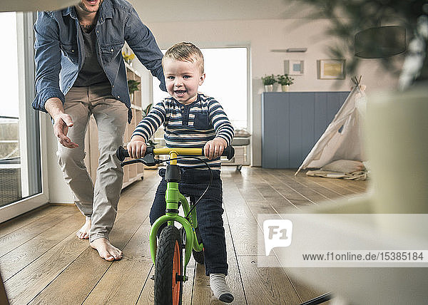 Father helping son riding with a balance bicycle at home