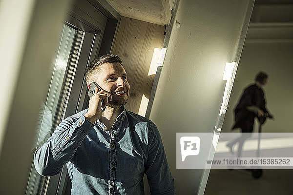 Young businessman talking on the phone while colleague using kickboard oin background