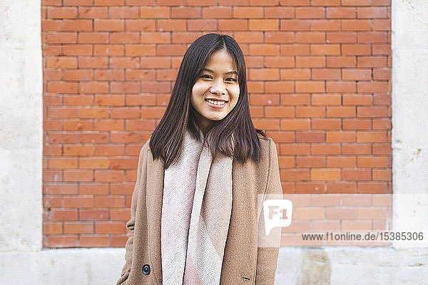 Porträt einer lächelnden jungen Frau an einer Ziegelmauer