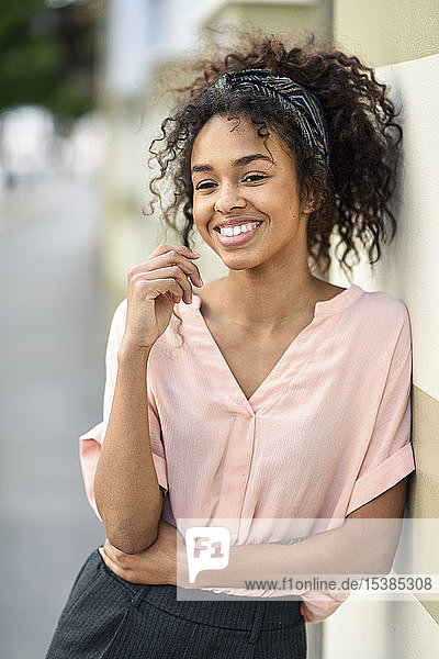 Smiling young woman leaning against a wall looking around