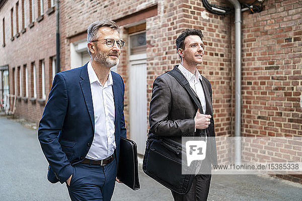 Zwei lächelnde Geschäftsmänner gehen an einem alten Backsteingebäude vorbei