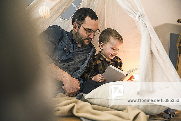 Father and son reading a book together in tent at home