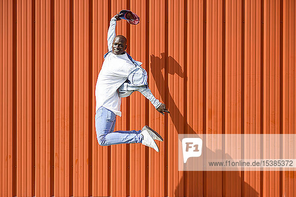 Mann in lässiger Jeansbekleidung springt vor orangener Wand in die Luft