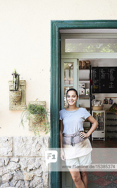 Porträt einer lächelnden Frau die an der Eingangstür eines Cafés steht
