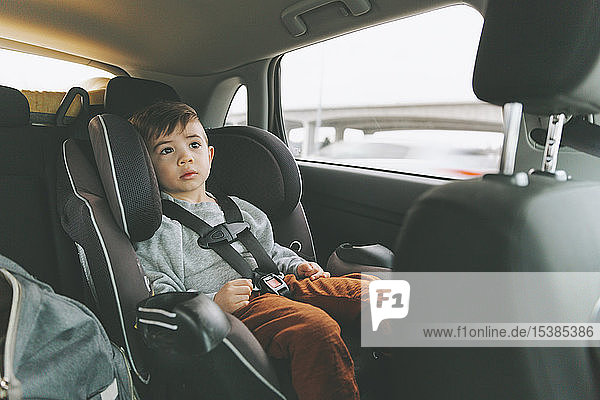 Little boy sitting in car on child's seat with fastened seat belt