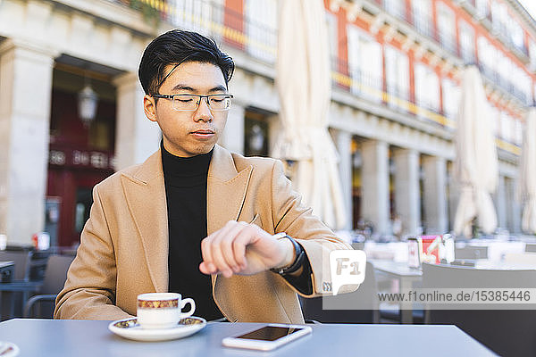 Spanien  Madrid  junger Mann überprüft die Uhrzeit in einem Café auf der Plaza Mayor