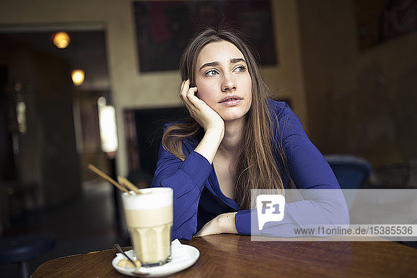 Junge Frau  die in einem Café am Tisch sitzt und zur Seite schaut