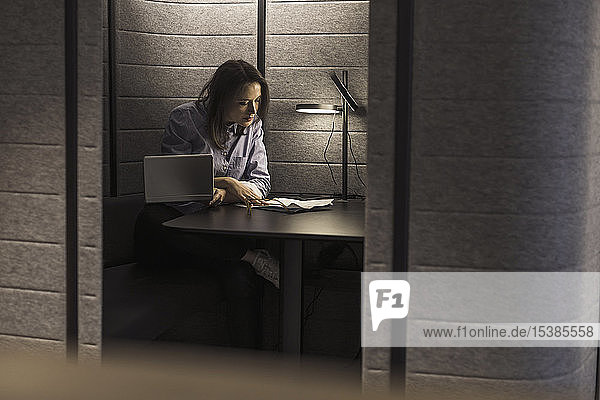 Geschäftsfrau  die mit Laptop und Dokumenten in einer Büronische arbeitet