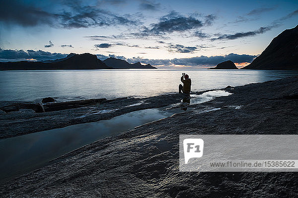 Norwegen  Lofoten  Haukland Beach  Mann sitzt auf Fels und baut Herz mit den Fingern