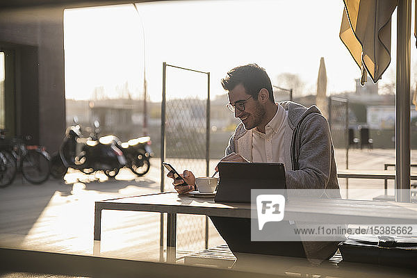 Junger Mann benutzt Handy und Tablet im Strassencafé