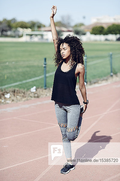 Sporty young woman stretching on tartan track