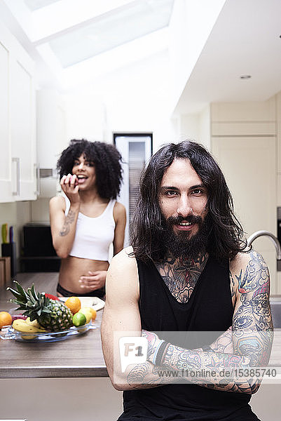 Porträt eines lächelnden tätowierten Mannes mit Freundin in der Küche