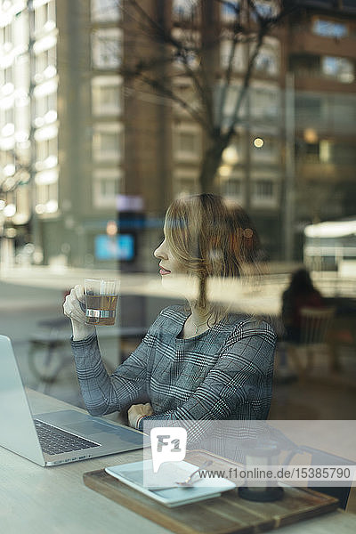 Reife Geschäftsfrau mit einem Laptop mit einem Glas Tee in einem Cafe