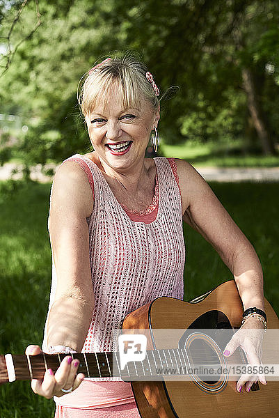Porträt einer glücklichen älteren Frau  die im Park Gitarre spielt