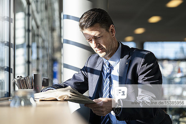 Geschäftsmann liest Zeitung am Fenster in einem Cafe