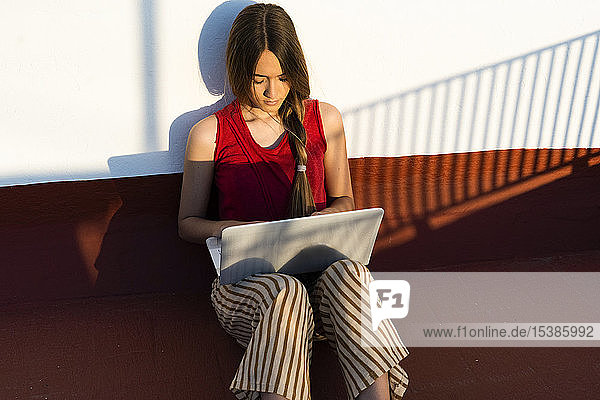 Teenagerin sitzt mit Laptop im Freien im Sonnenlicht