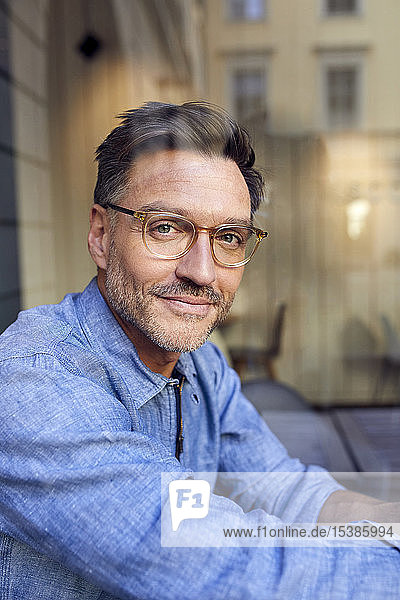 Porträt eines selbstbewussten Brillenträgers hinter einer Fensterscheibe