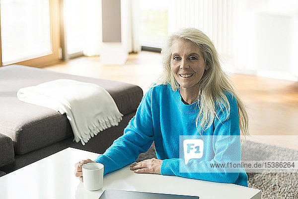 Porträt einer lächelnden reifen Frau mit Tasse Kaffee zu Hause