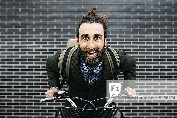 Porträt eines glücklichen Mannes mit E-Bike an einer Ziegelmauer