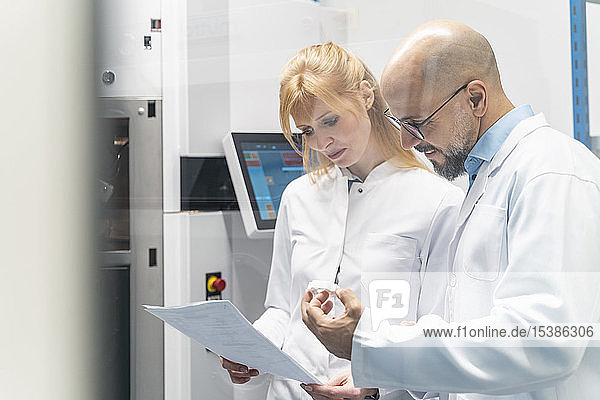 Two technicians wearing lab coats looking at plan