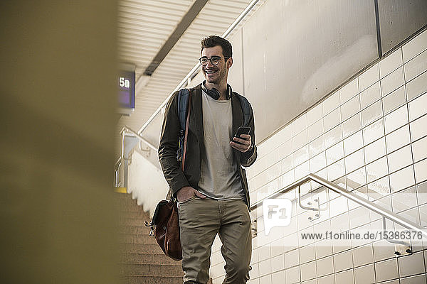 Lächelnder junger Mann mit Handy geht am Bahnhof die Treppe hinunter