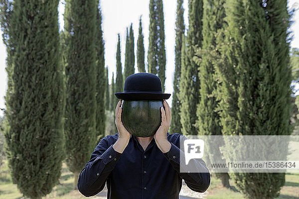 Italy  Tuscany  man surrounded by cypresses wearing a bowler hat holding a melon