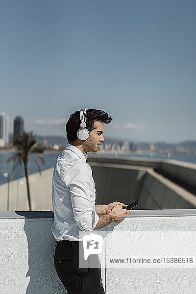 Profil eines Geschäftsmannes  der mit Kopfhörer und Smartphone auf der Dachterrasse Musik hört