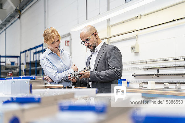 Businessman and businesswoman examining workpiece in factory