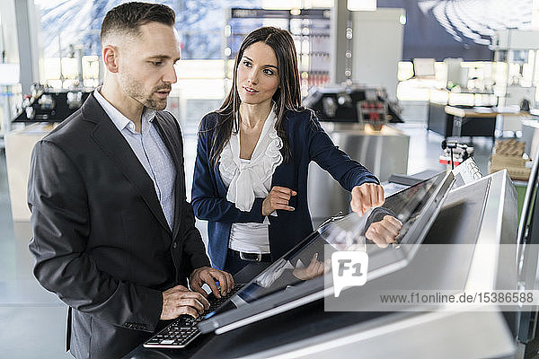 Businessman and businesswoman talking at a machine in a modern factory
