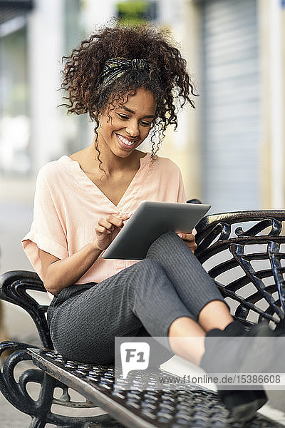 Lächelnde junge Frau sitzt auf einer Bank und benutzt ein Tablett