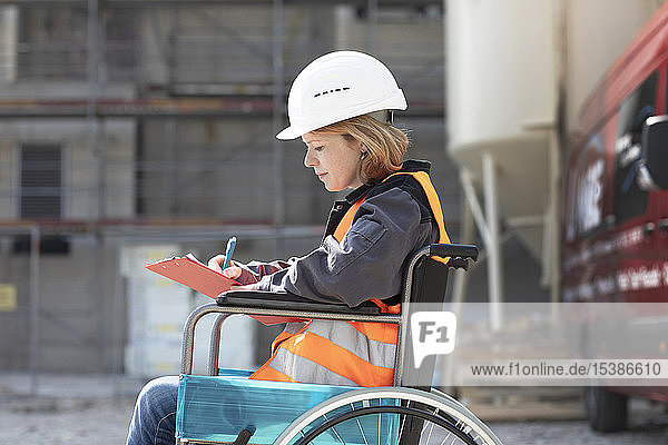 Frau mit reflektierender Weste und Schutzhelm sitzt im Rollstuhl und macht Notizen