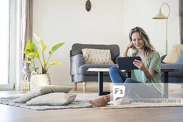 Smiling woman sitting on the floor at home using tablet