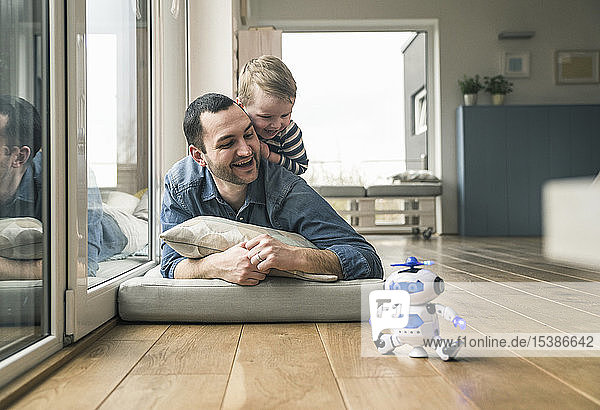 Excited father and son lying on a mattress at home watching a toy robot