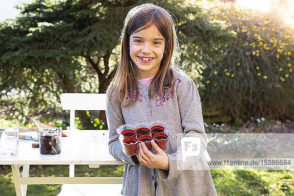 Portrait of happy little girl with flowerpots in the garden