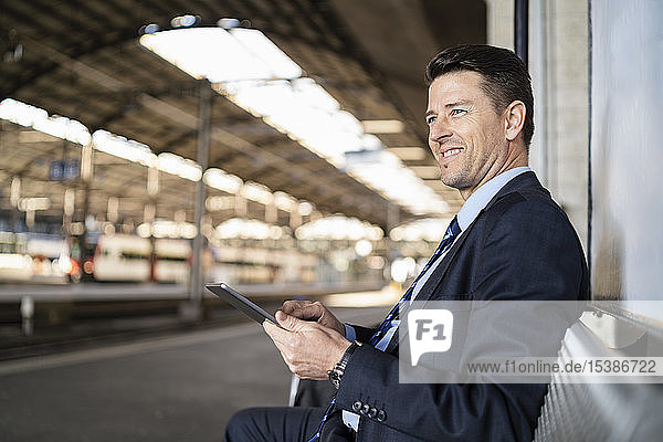 Smiling businessman with tablet waiting on station platform