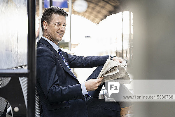 Smiling businessman reading newspaper on station platform