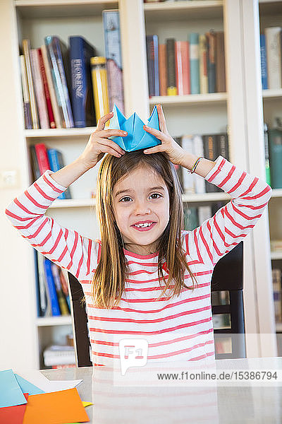 Portrait of smiling girl putting on selfmade paper hat at home