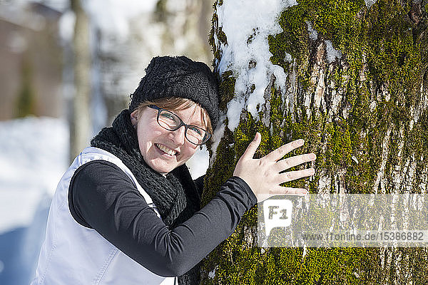 Porträt einer lächelnden Frau  die im Winter einen Baum umarmt