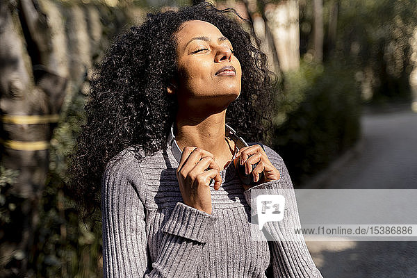 Porträt einer Frau mit Kopfhörern  die mit geschlossenen Augen die Sonne genießt