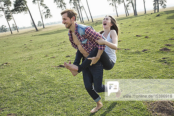 Happy young man carrying girlfriend piggyback on meadow
