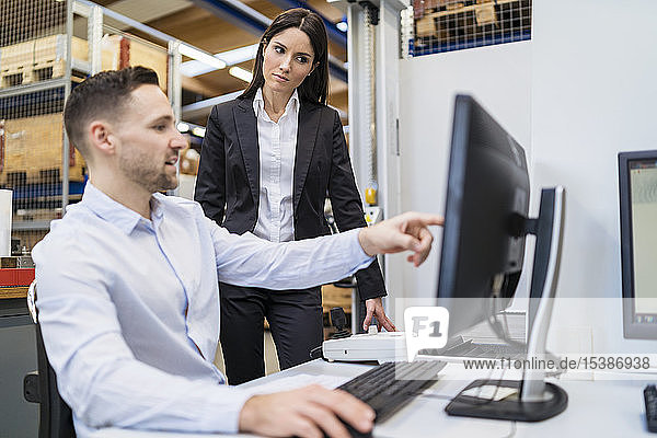 Businessman and businesswoman talking at computer in modern factory