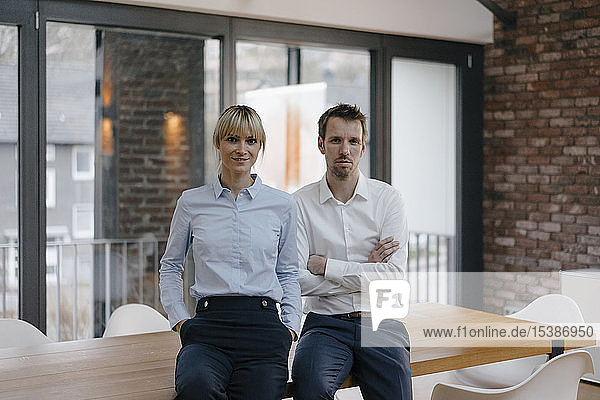 Successful businessman and woman standing in office  with arms crossed