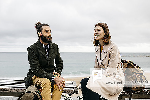 Lächelndes Paar sitzt auf einer Bank an der Strandpromenade und unterhält
