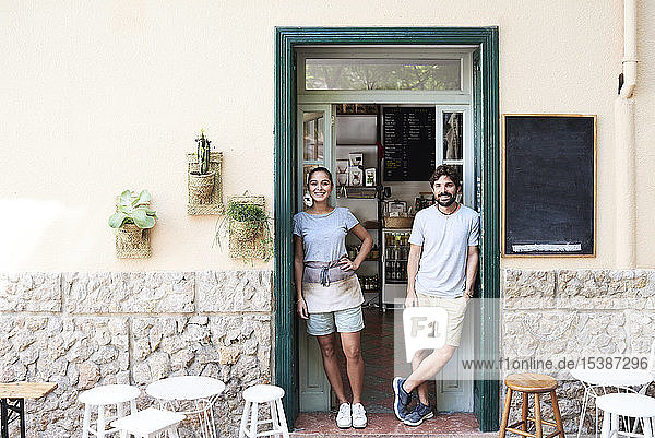 Porträt eines lächelnden Mannes und einer lächelnden Frau  die an der Eingangstür eines Cafés stehen
