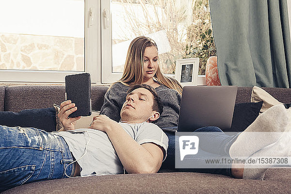 Young couple relaxing on sofa and using notebook  smartphone and ebook reader