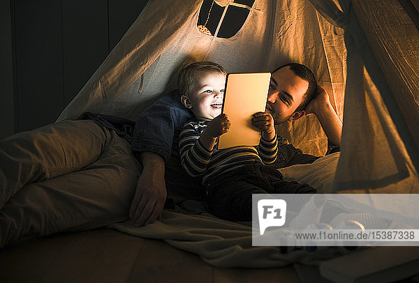 Father and son sharing a tablet in a dark tent at home