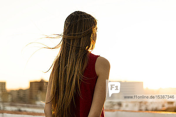 Rückansicht eines Teenager-Mädchens auf der Dachterrasse der Stadt bei Sonnenuntergang