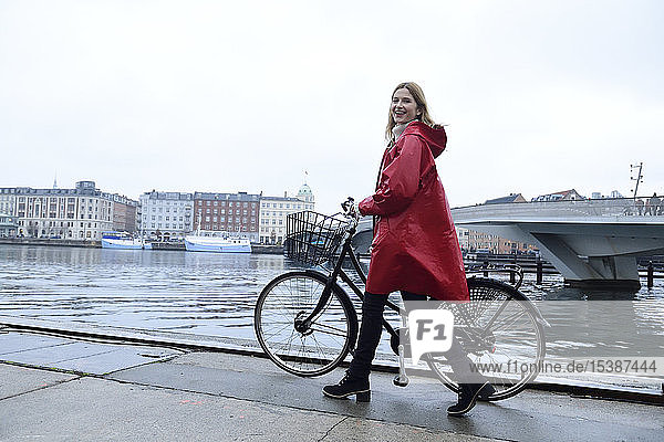 Dänemark  Kopenhagen  glückliche Frau schiebt bei Regenwetter Fahrrad im Stadthafen