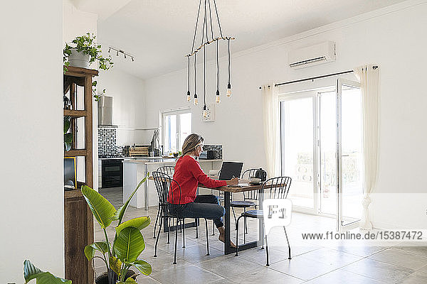 Frau benutzt Laptop auf dem Esstisch im modernen Haus