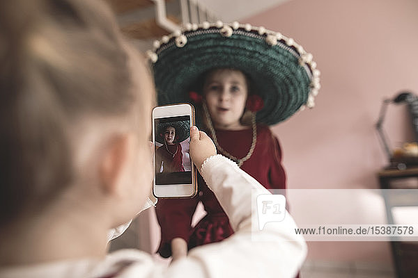 Little girl taking picture of dressed up sister with smartphone